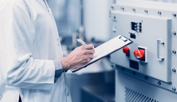 Lab technician taking note of measurements in front of machinery